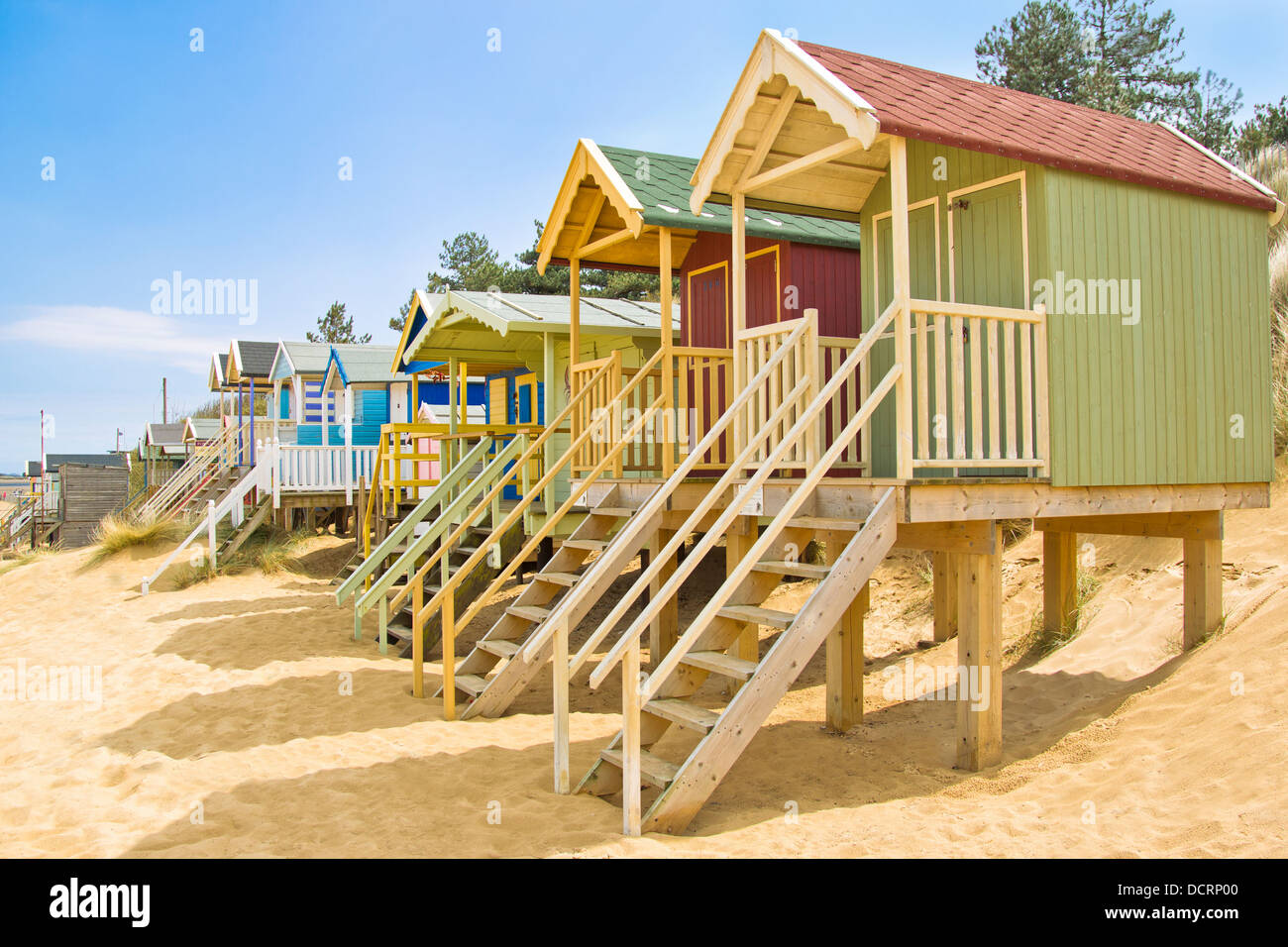 Row of colourful beach huts in golden sand on beach with blue sky Stock Photo