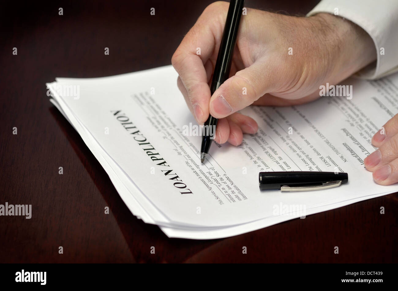 Business man signing loan application with black pen on desk Stock Photo