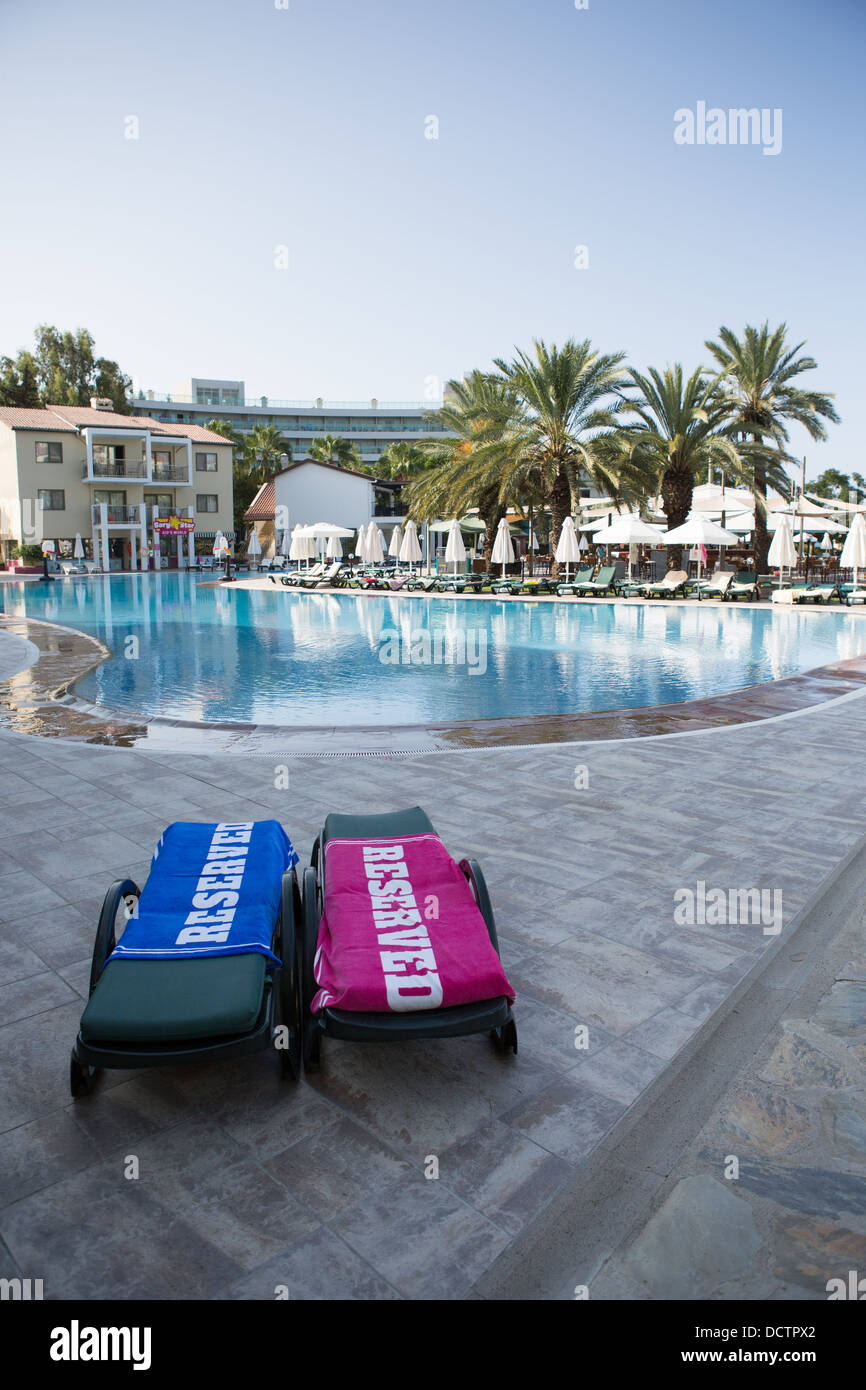 Two sun loungers with 'reserved' towels next to a hotel swimming pool Stock Photo