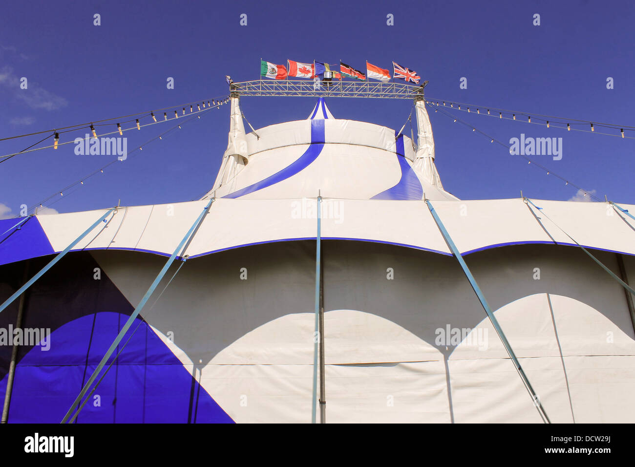 Blue and white circus tent with different country flags, blue sky and cloudscape background. Stock Photo
