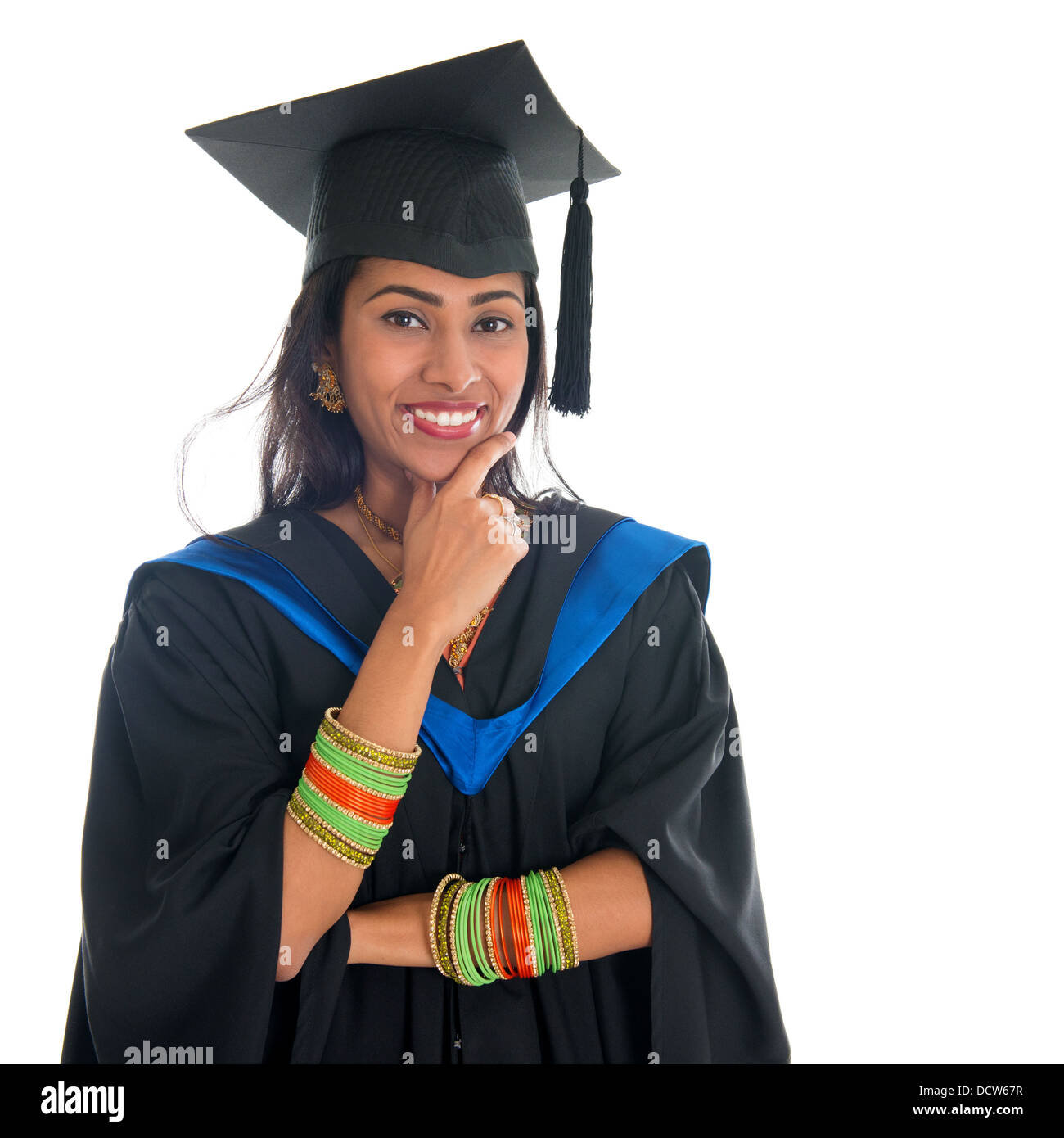 Happy Indian university student in graduation gown and cap thinking. Portrait of mixed race Asian Indian and African American female model standing isolated on white background. Stock Photo