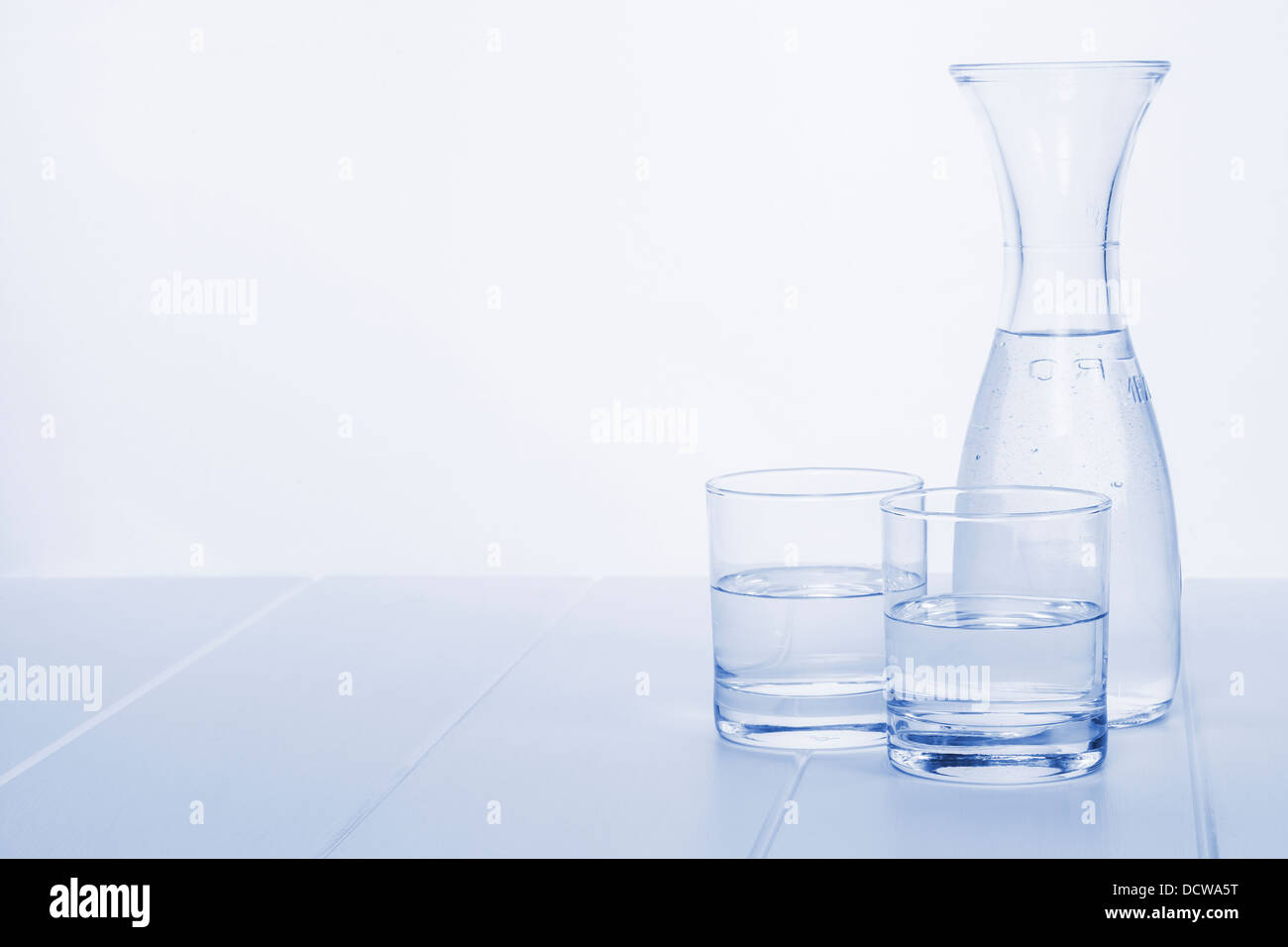 Water Carafe and Two Glasses - a carafe of water on a table with two glasses, blue toned, horizontal. Stock Photo