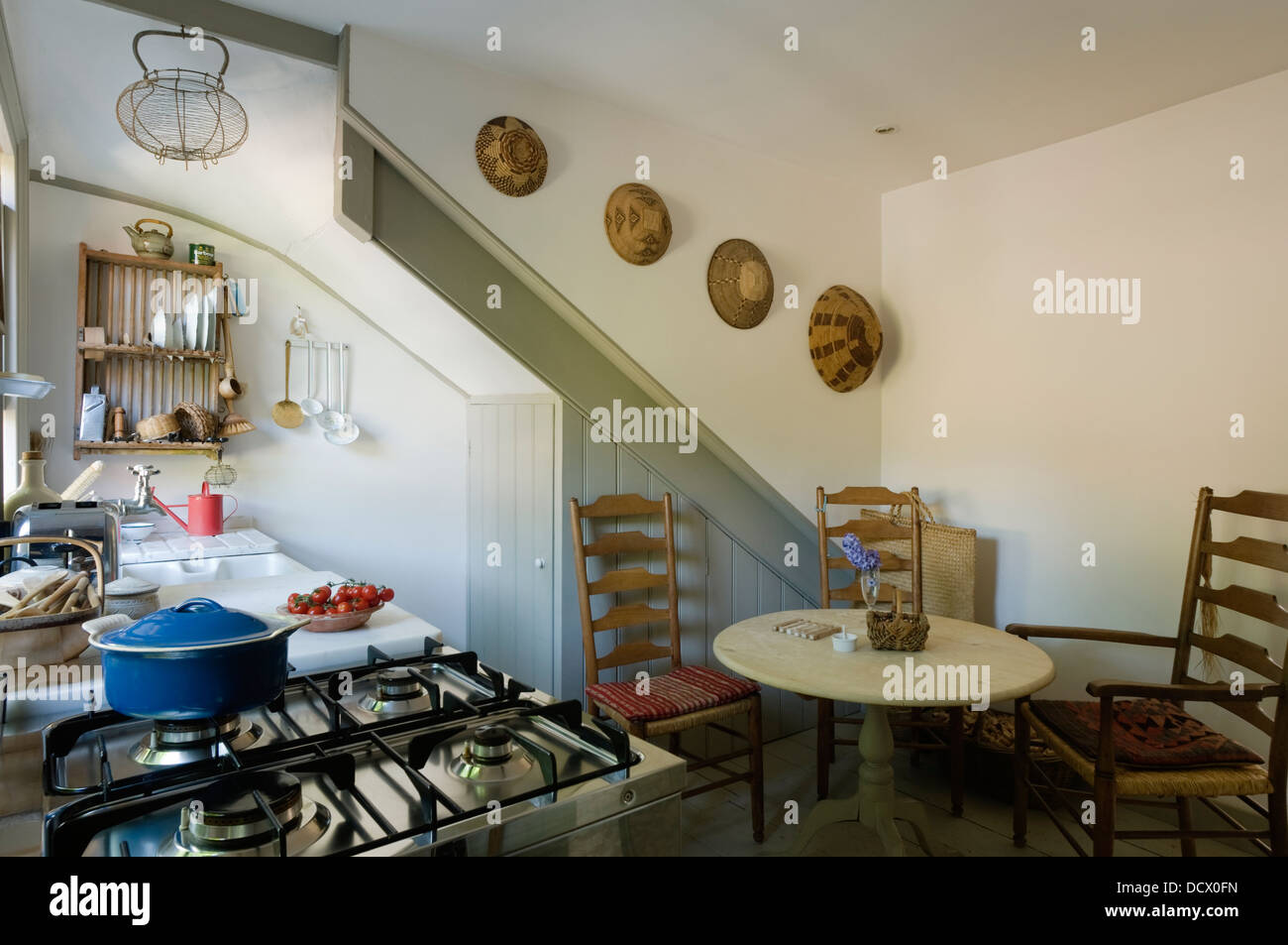 Ladderback chairs and storage cupboards in kitchen with plate rack and collection of African bowls Stock Photo