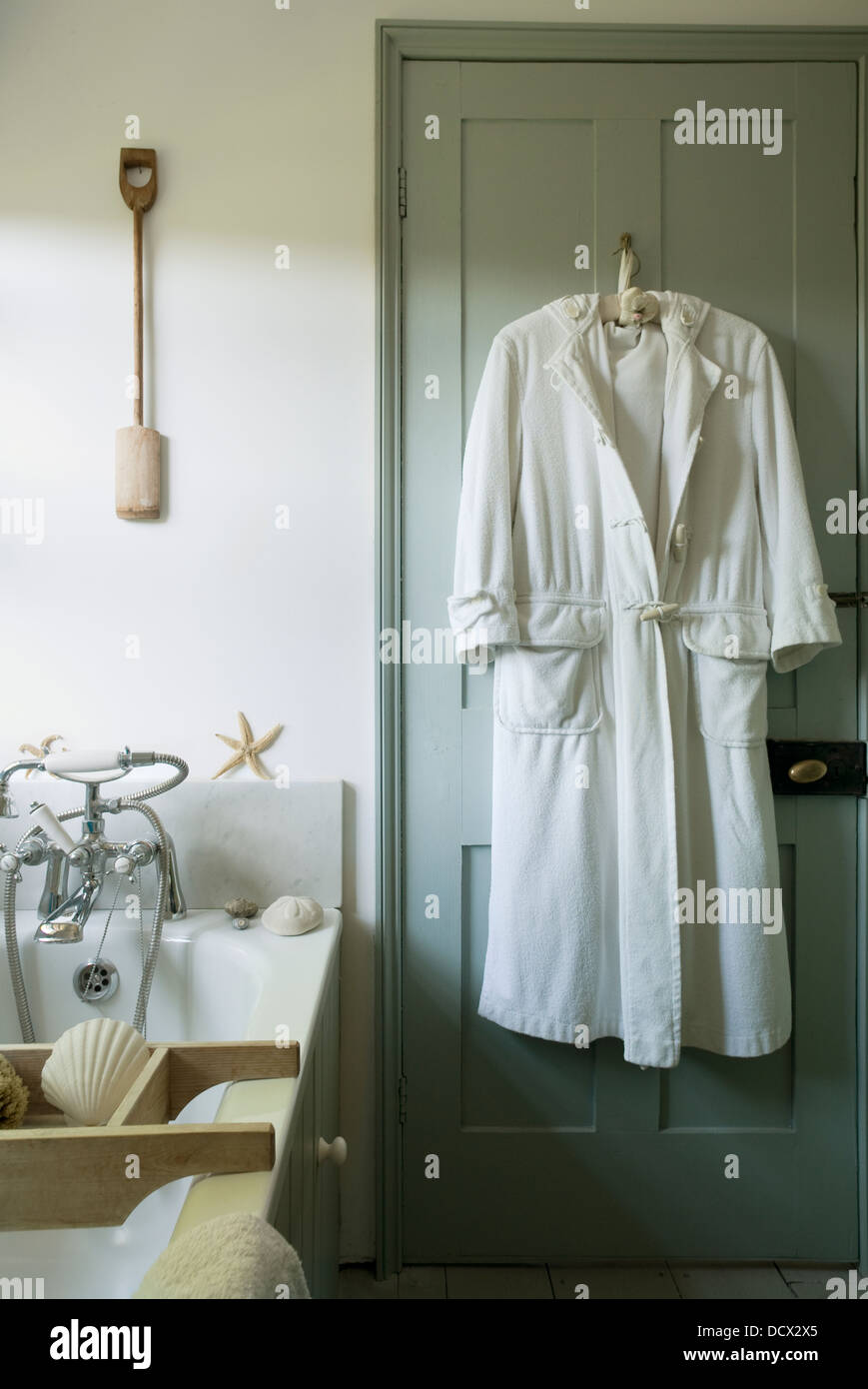 White bathrobe hangs on back of pastel beach house bathroom door Stock Photo