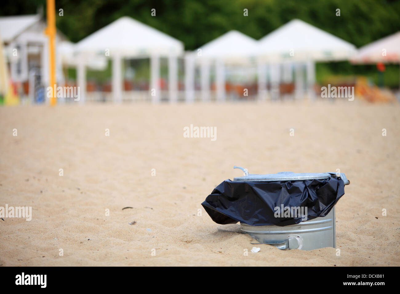 Gray metal garbage bin or trash can with a plastic bag inside beach