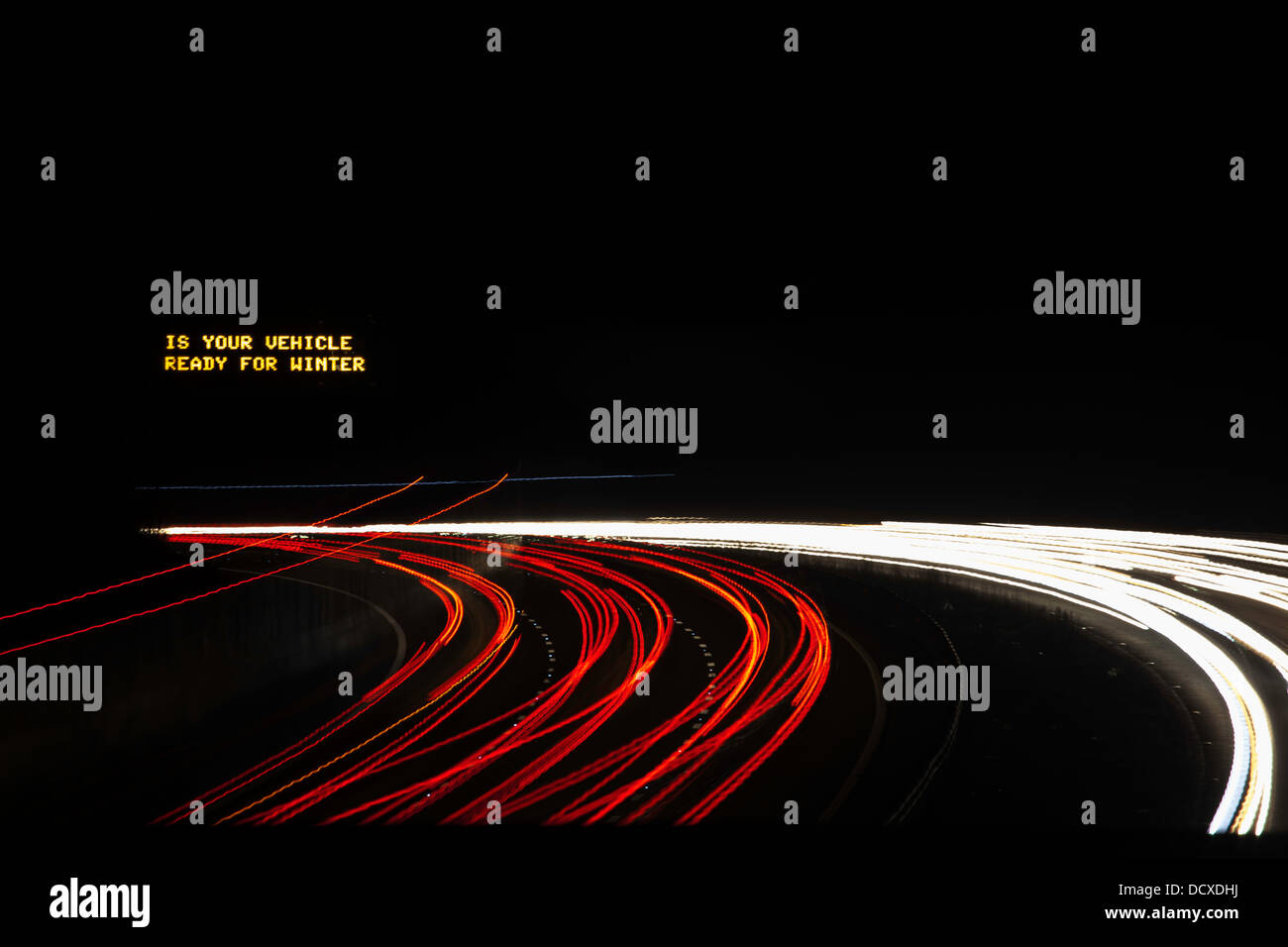 Light trails on motorway at night with warning sign "is your vehicle ready for winter" England, UK Stock Photo
