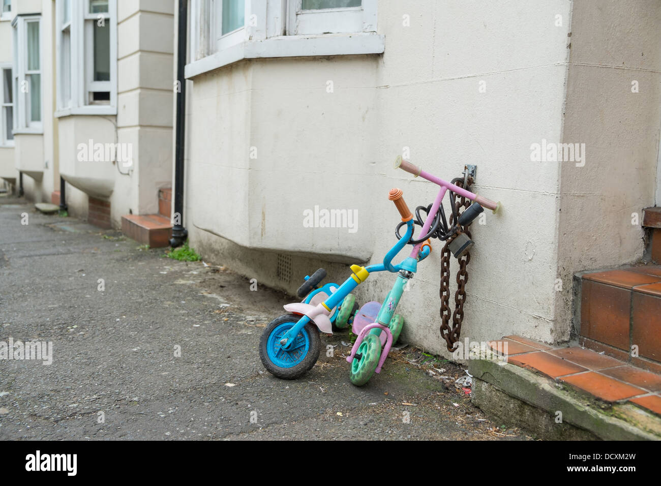 Two childrens scooters chained up in the street Stock Photo