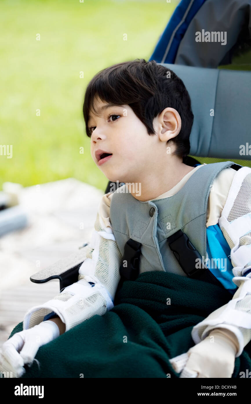 Four year old boy disabled with cerebral palsy sitting outdoors Stock Photo