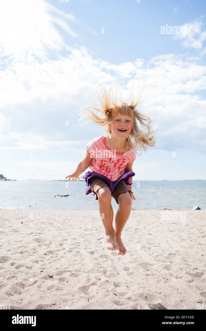 Cute happy young girl jumping in the sand at the beach in summer Stock