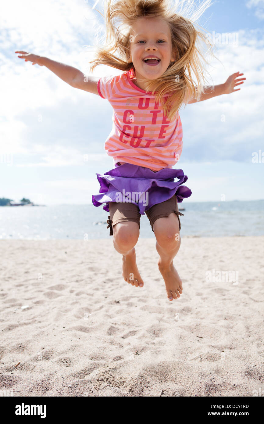 Cute happy young girl jumping in the sand at the beach in summer Stock