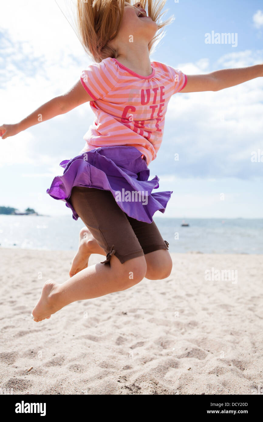 Cute happy young girl jumping in the sand at the beach in summer Stock