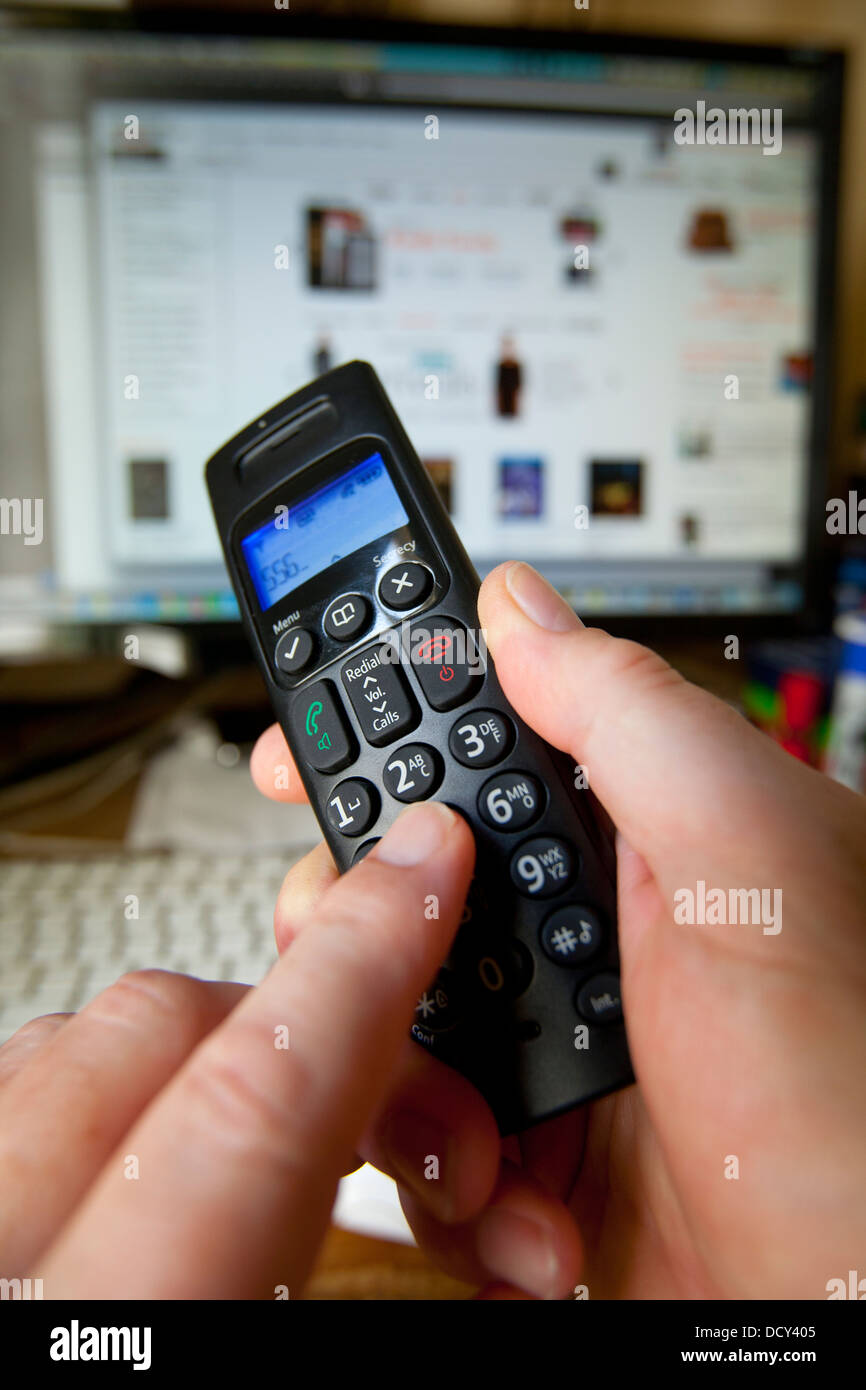 Hand Holding Dialing Phone Handset in front of Computer with Amazon on