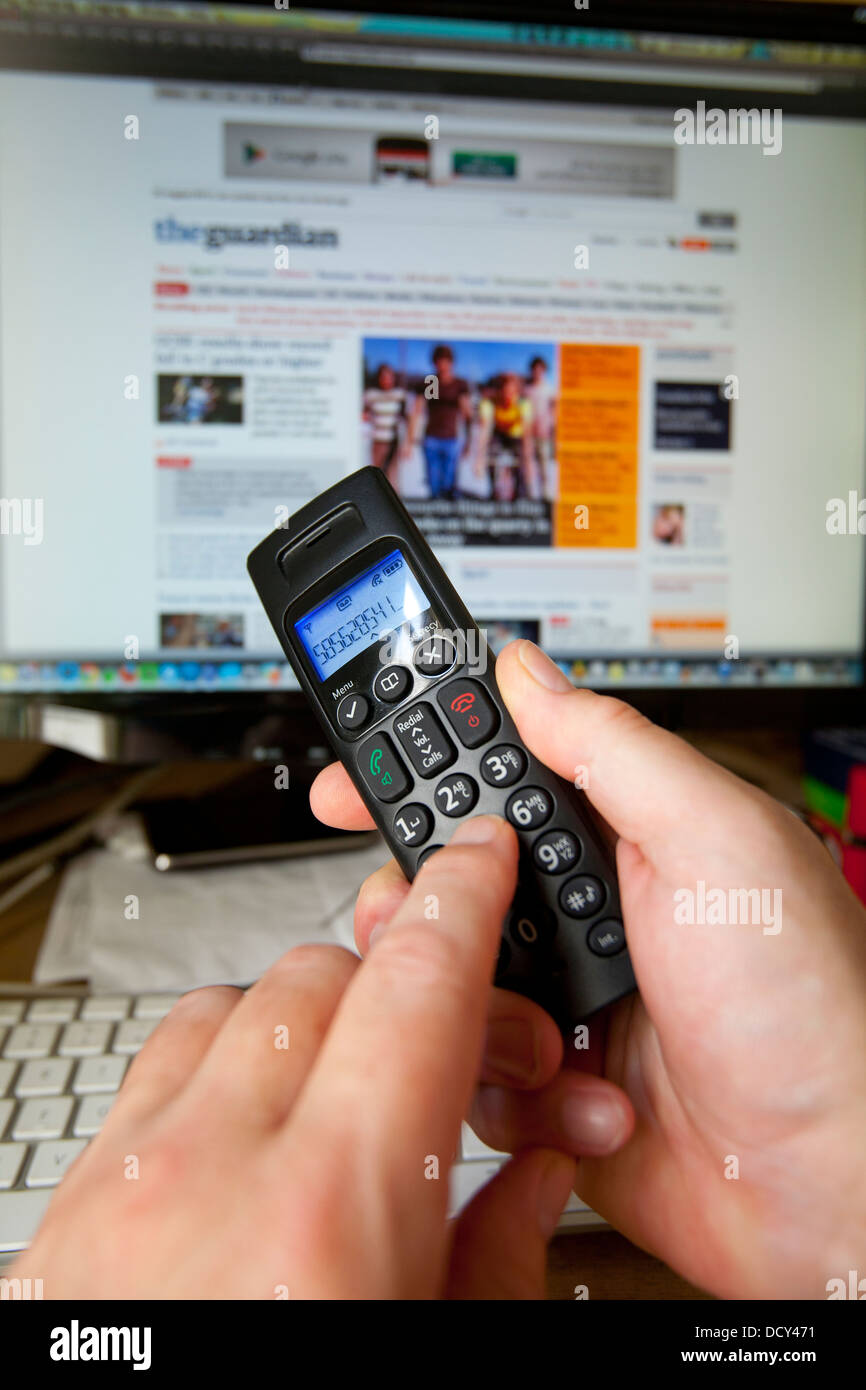 Hand Holding Dialing Phone Handset in front of Computer with Guardian