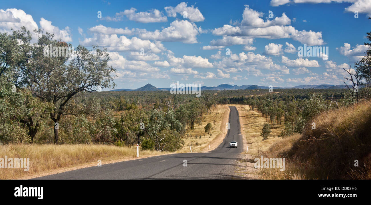 Outback / bush / country road with eucalyptus trees either side and mountains in distance and car on road Queensland Australia Stock Photo