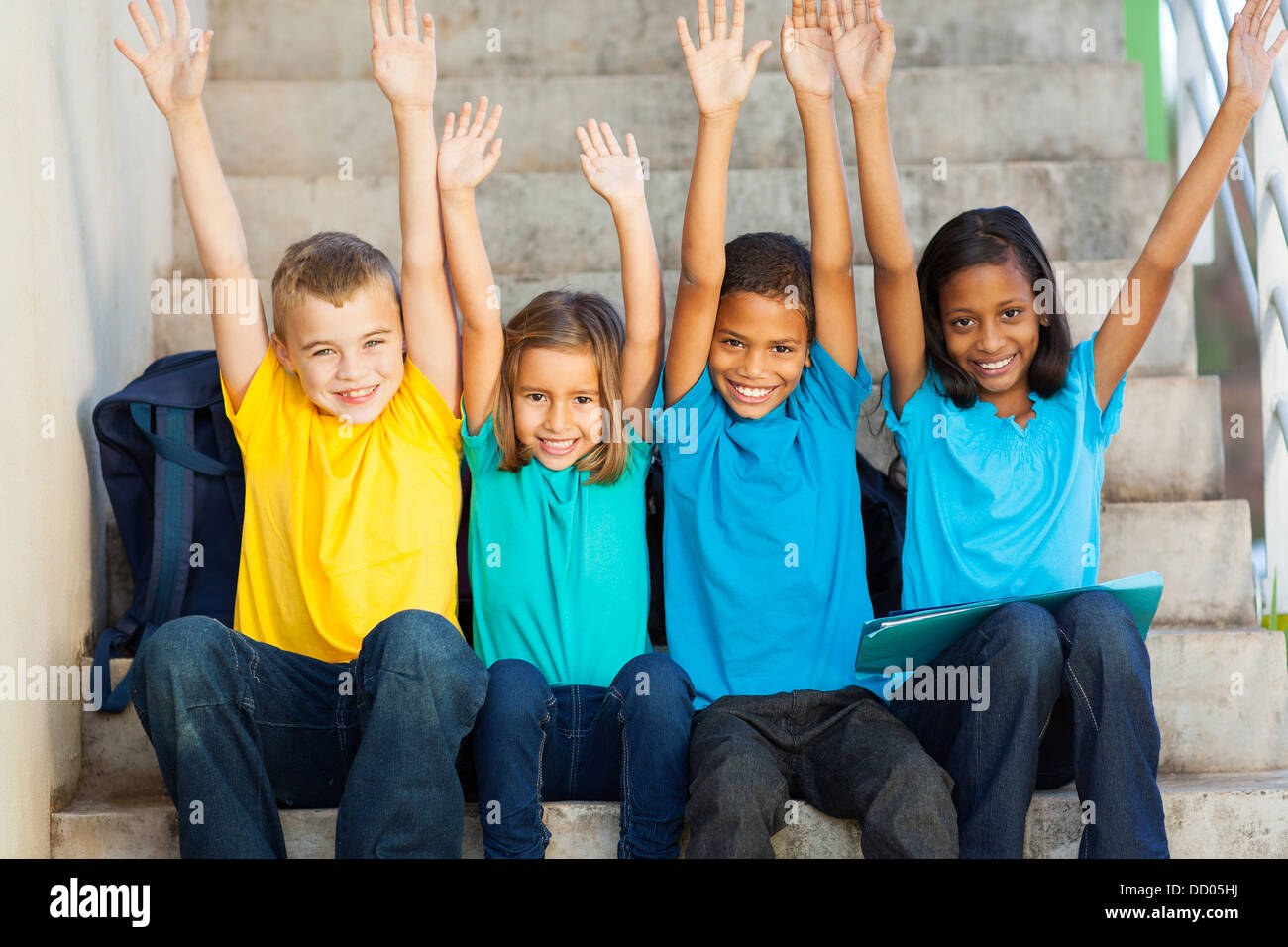 group of happy primary students with hands raised sitting outdoors Stock Photo