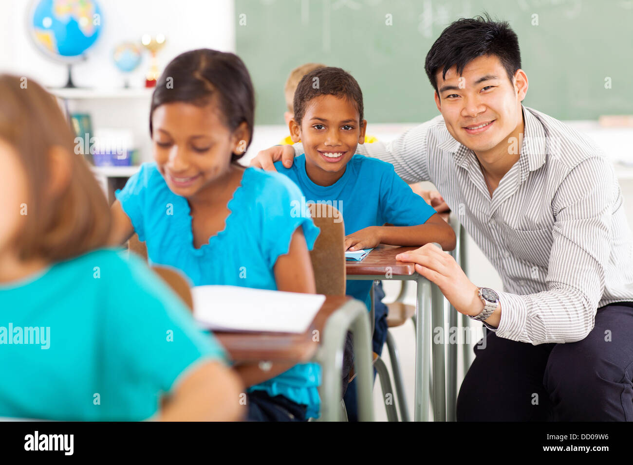 portrait of happy primary teacher helping student in classroom Stock Photo