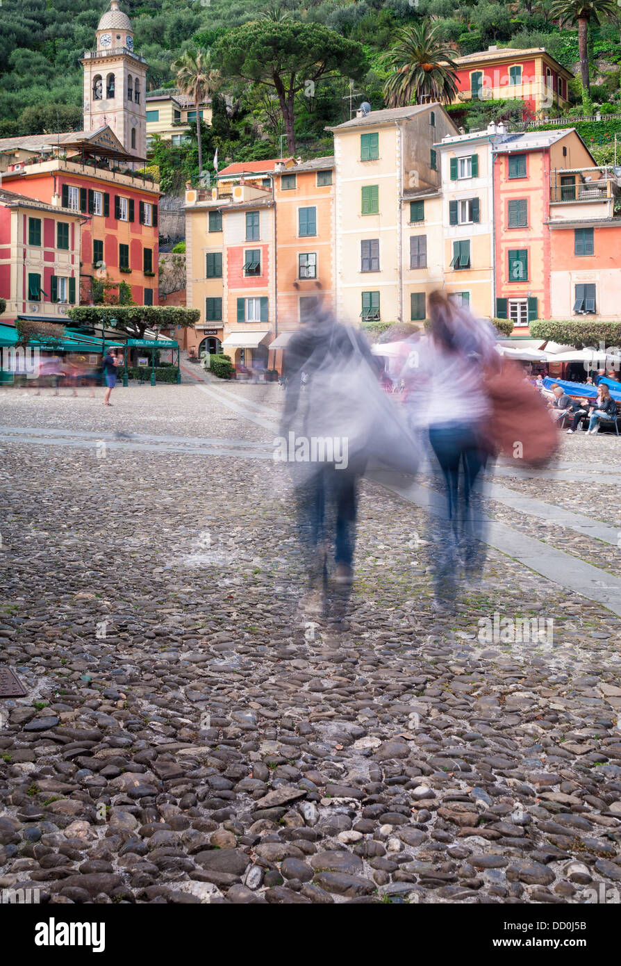 Portofino harbour front with motion blur of tourists, brightly coloured apartment buildings, outdoor cafes, church and belltower Stock Photo