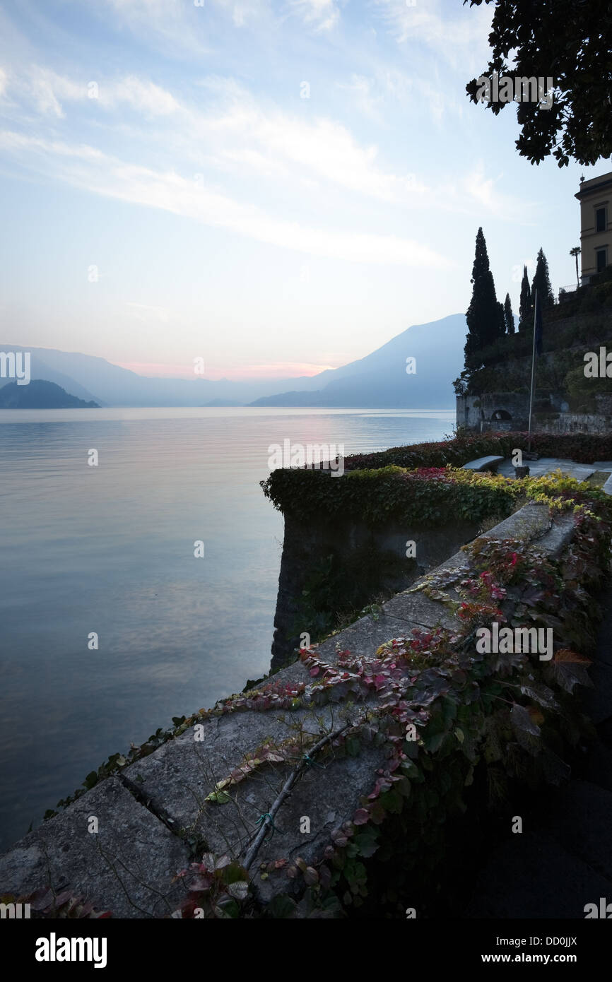 Tranquil scene overlooking Lake Como at sunset, blue and pink sky, still waters, cypress trees,  wall with trailing ivy with aut Stock Photo