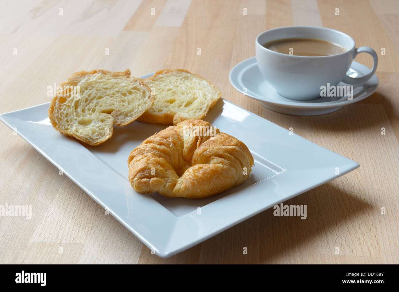 Croissant's on a white rectangular plate on a wooden table with cup and saucer containing white coffee breakfast morning coffee Stock Photo