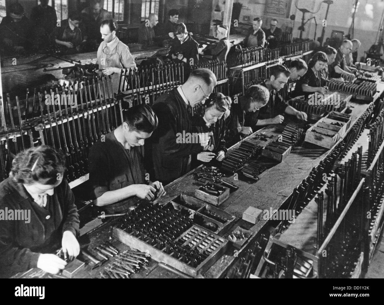 German women and foreign men assemble various small arms in an arms factory in December 1944, place unknown. The employment of women as workers in all sectors ensured, as is pictured here in the arms industry, adequate supply at the front. The Nazi Propaganda! on the back of the picture is dated 11 December 1944: 'Rapid-fire weapons in precision work. In German arms factories, thousands of machine guns, rapid-fire and automatic rifles, and pistols are assembled daily and immediately sent out to the troups at the front. Our picture shows: German women and foreign workers assemble the precision  Stock Photo
