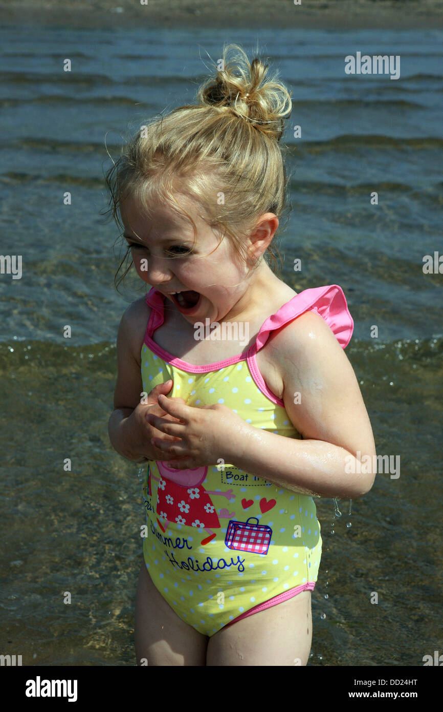 Four year old girl screaming with delight as she is splashed by water on entering the sea at Troon, Ayrshire Scotland Stock Photo