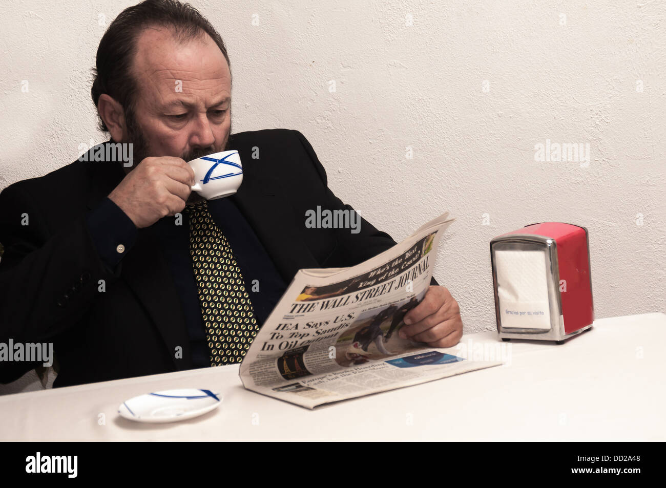 A businesman drinks his coffee while reading a business newspaper Stock Photo