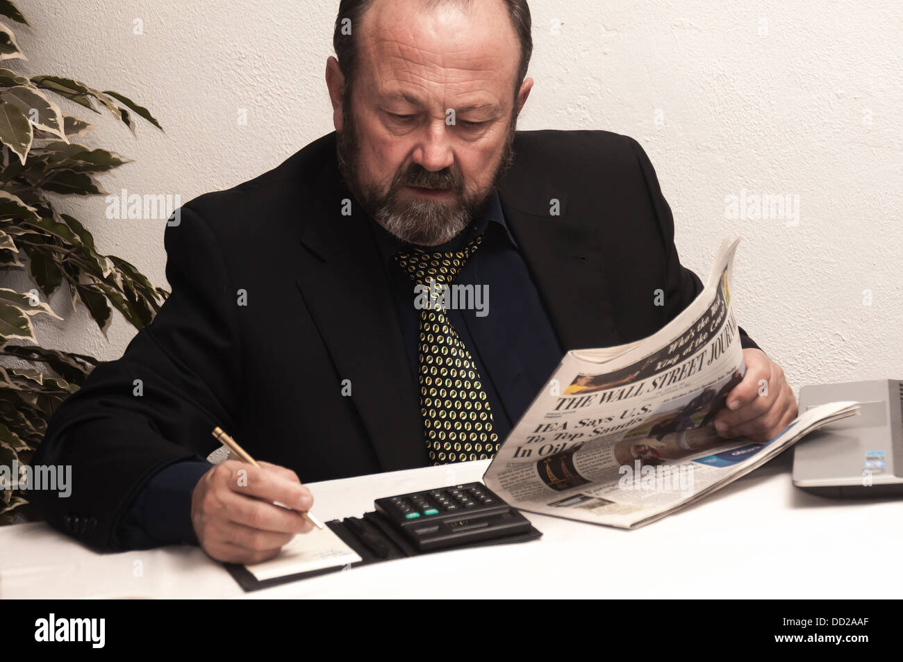 A business is looking concerned while he uses his calculator and reads a newspaper Stock Photo