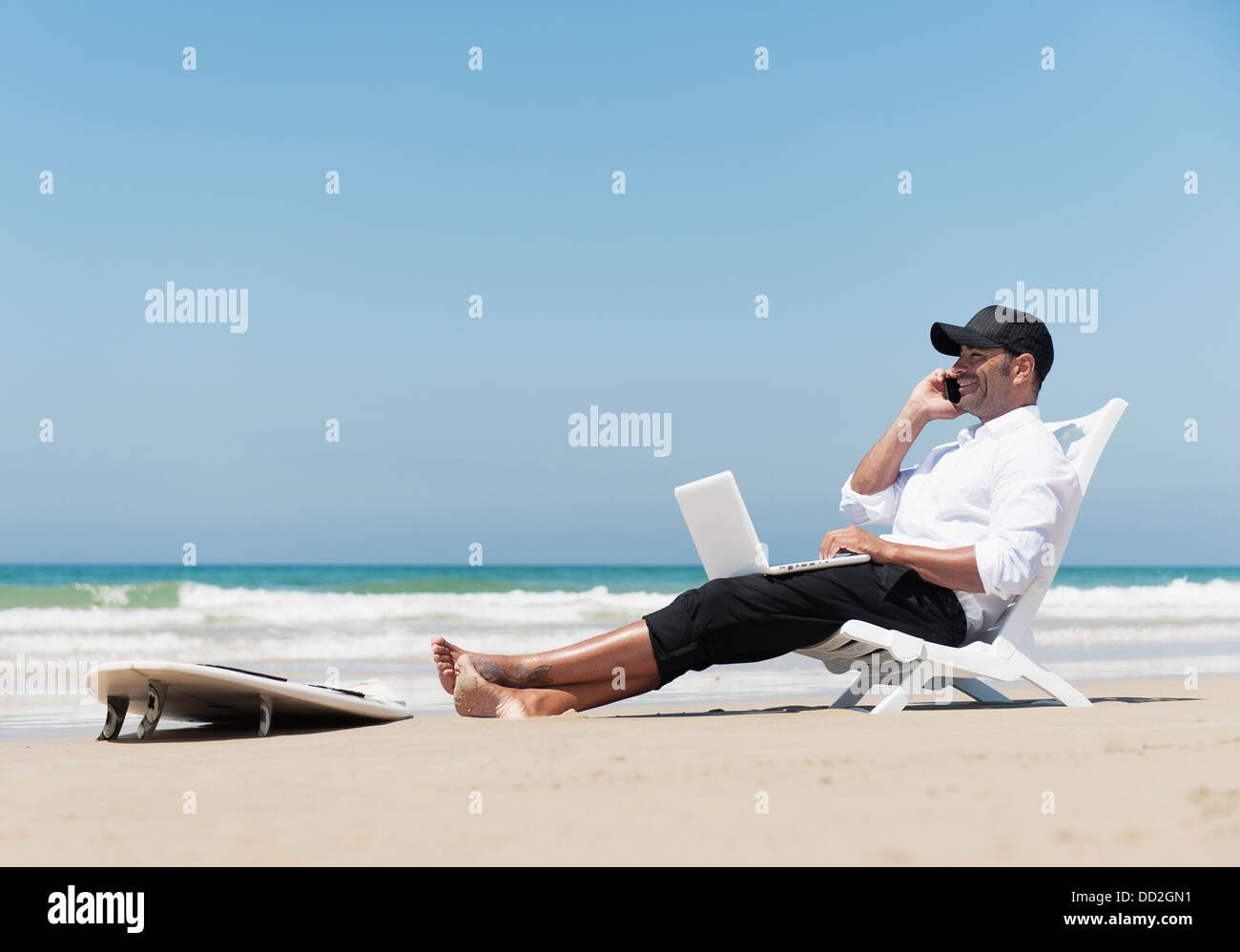 A Businessman In A Chair On The Beach Working On A Laptop Computer Talking On The Phone With His Surfboard Sitting At His Feet Stock Photo Alamy