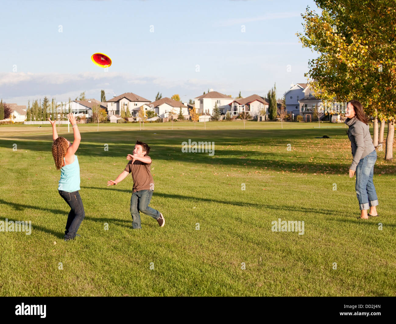 Mother Throwing Flying Disc To Children In A Park; Beaumont, Alberta, Canada Stock Photo