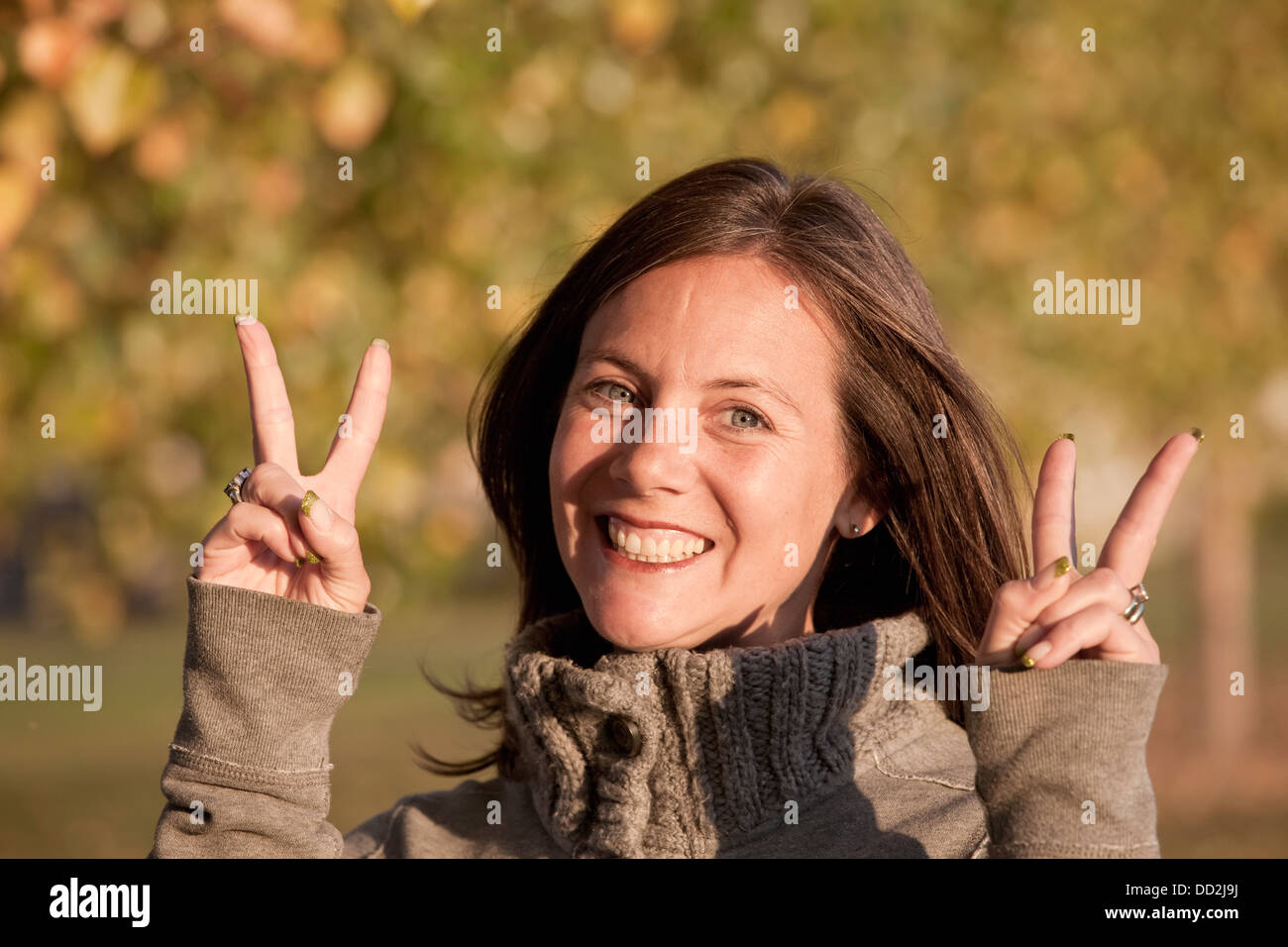 A Woman Giving A The Peace Symbol In A Park In Autumn; Beaumont, Alberta, Canada Stock Photo