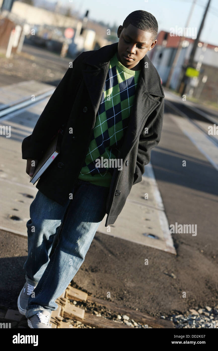 Teenage Boy Holding A School Book And Walking On Train Tracks; Portland, Oregon, United States of America Stock Photo