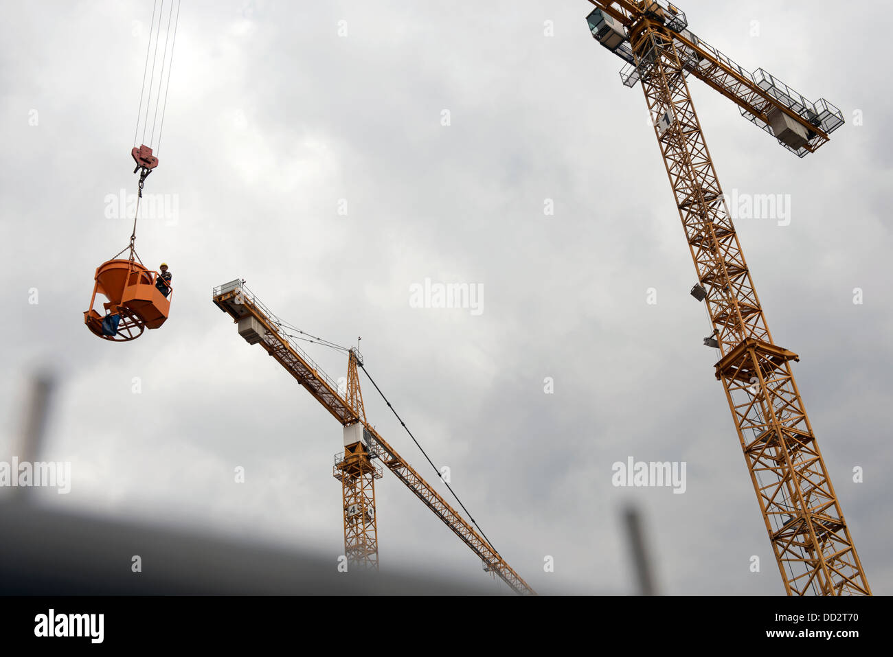 Workman operating a concrete bucket lifted onto a construction site by tower crane Stock Photo