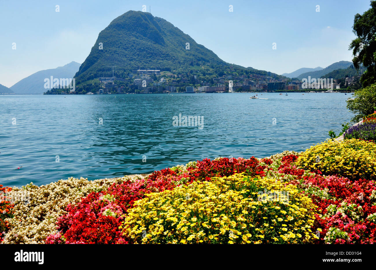 Switzerland - lake Lugano - Lugano town - colourful gardens beside the lake - view across the lake to Monte Bre - sunlight Stock Photo