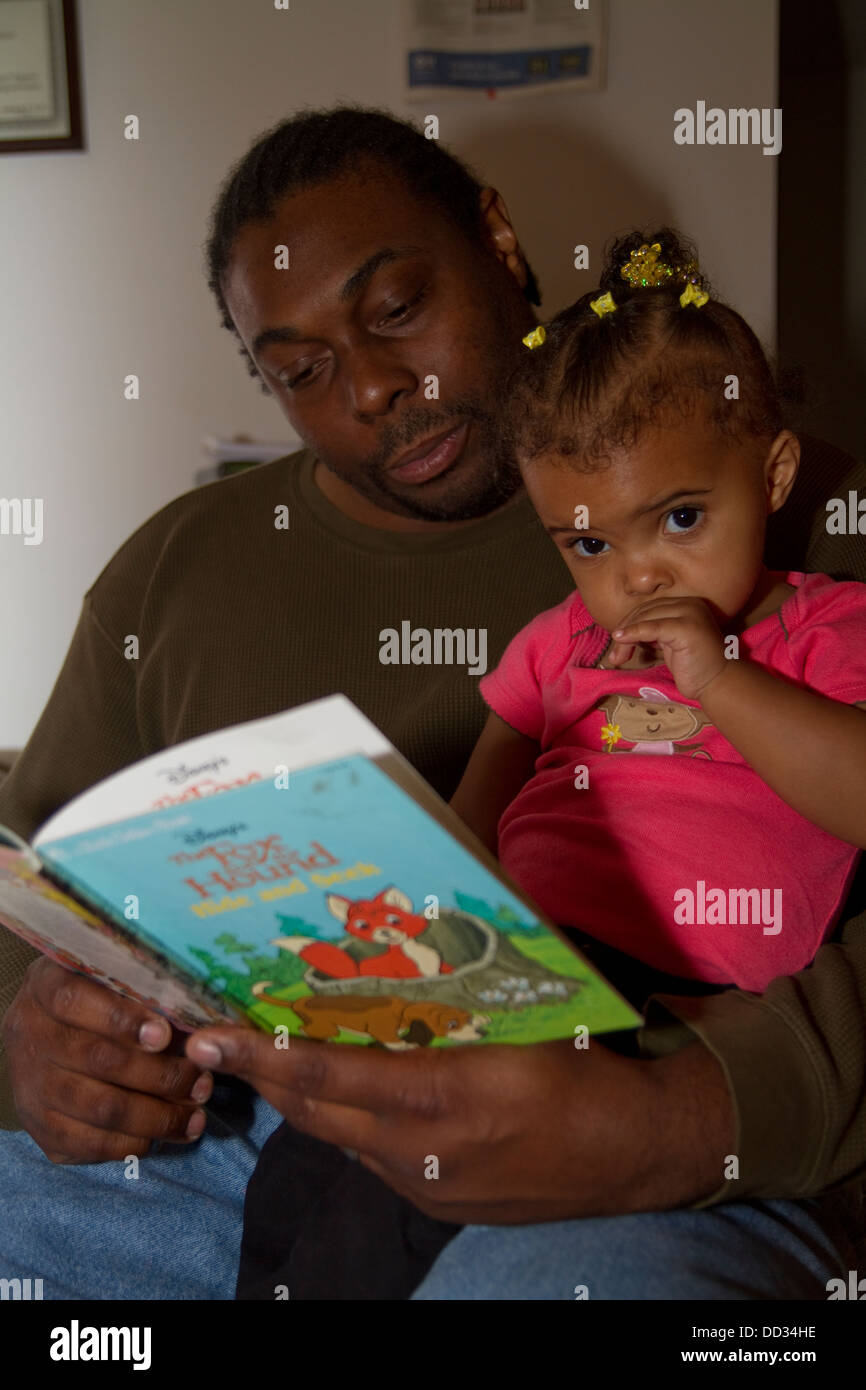 African-American male former inmate reading to his young daughter. This inmate managed to get a degree after his release. Stock Photo