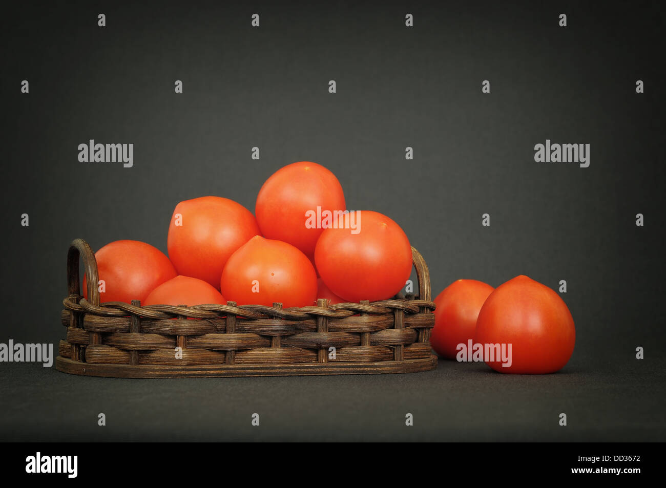 Small red tomatoes in a basket on dark table Stock Photo - Alamy