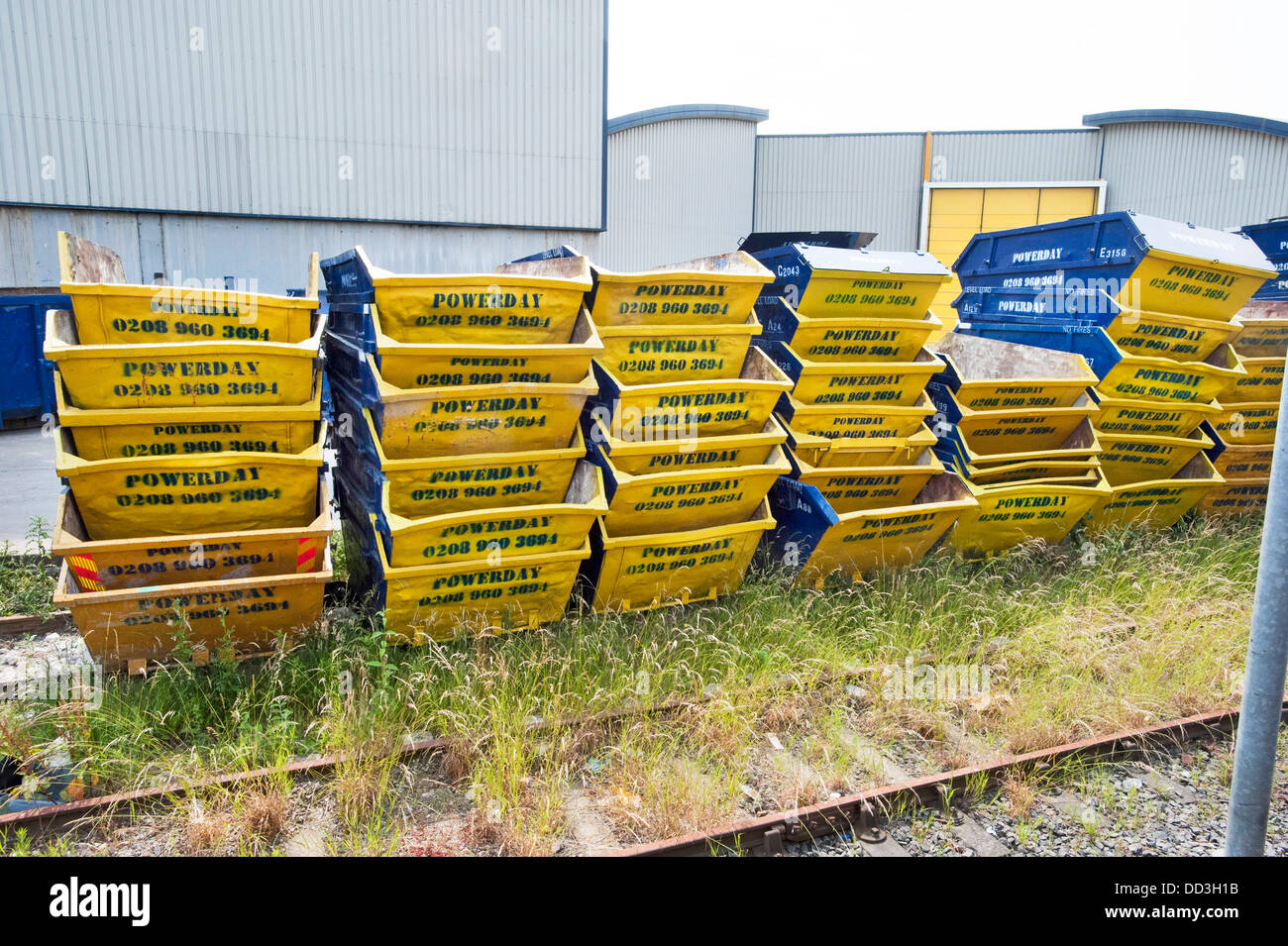 Stacks of piled up Yellow and Blue Rubbish 'Powerday' Skips, some Eight deep stand in a recycling yard by a railway line in Willesden, North London Stock Photo