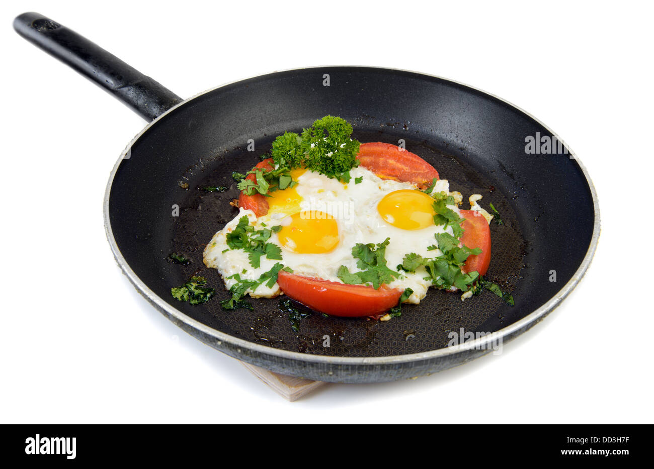 Fried eggs with tomato and herbs on kitchen pan isolated on white Stock Photo