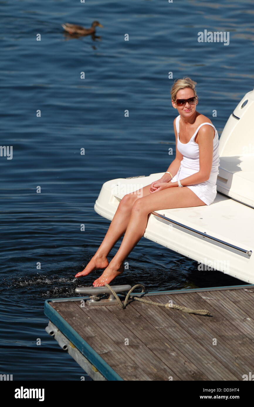 A beautiful woman sits on the end of a boat with her feet in the water, Luss, Loch Lomond, Scotland, UK Stock Photo