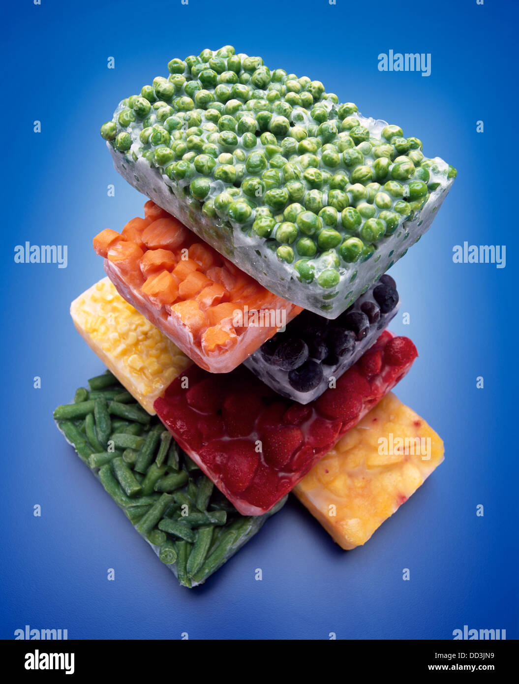 A large stack of frozen blocks of food; green peas, carrots, blackberries, corn, strawberries, peaches and green beans. Stock Photo