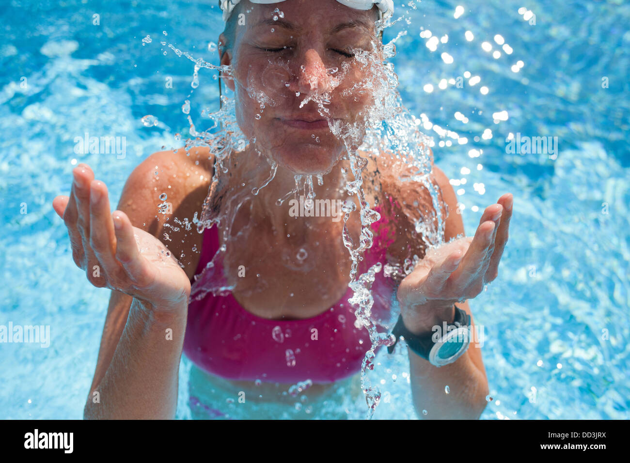 Happy female swimmer splashing water in face with eyes closed while in ...