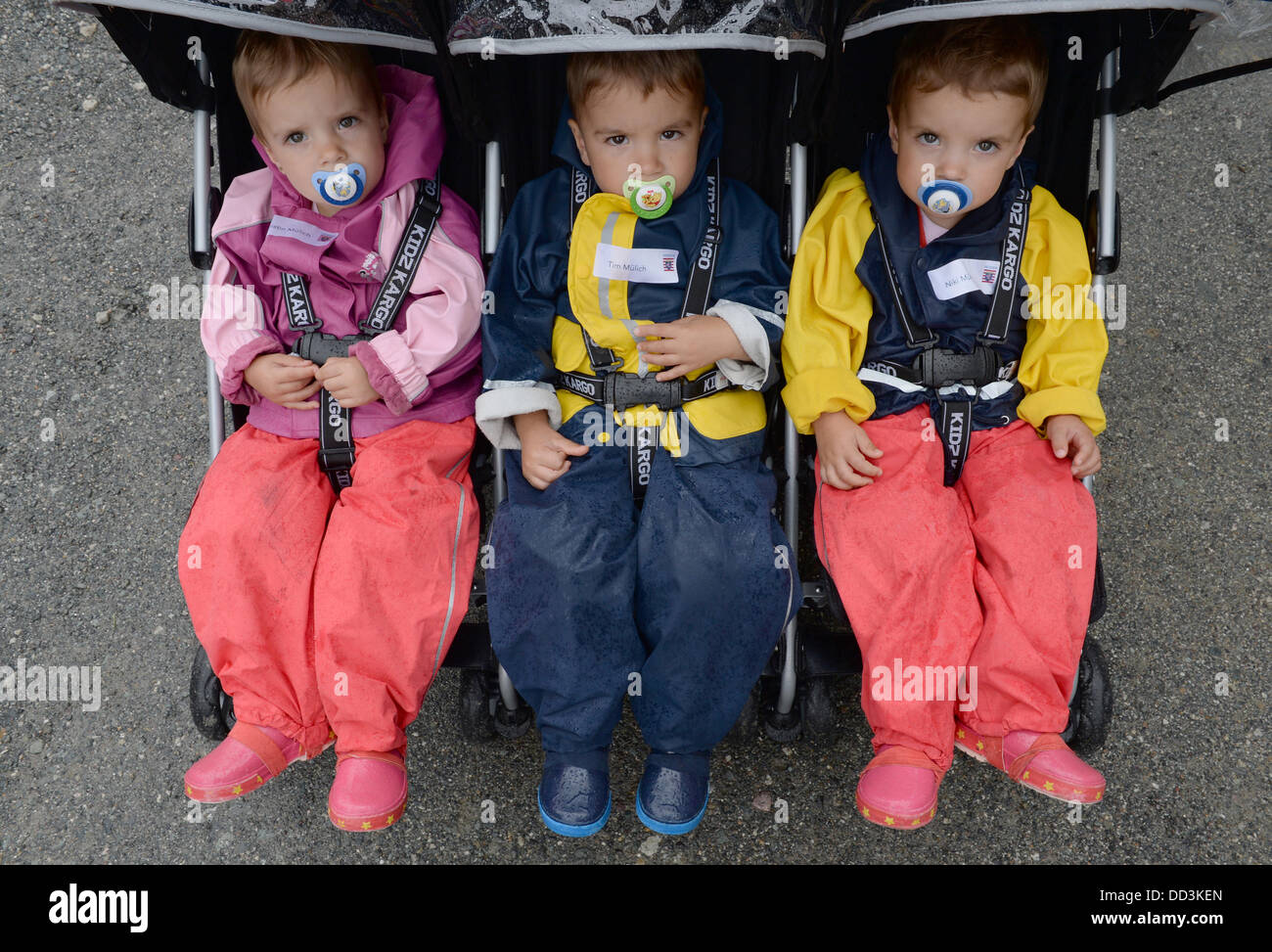 The triplets Christin (L-R), Tim and Niki sit in a carriage at the Triplet meeting held at Hessen Park on a rainy day in Neu-Anspach, Germany, 25 August 2013. The governor of Hesse is a godfather for all children of multiple births and hosts an event each year for them. Photo: ARNE DEDERT Stock Photo