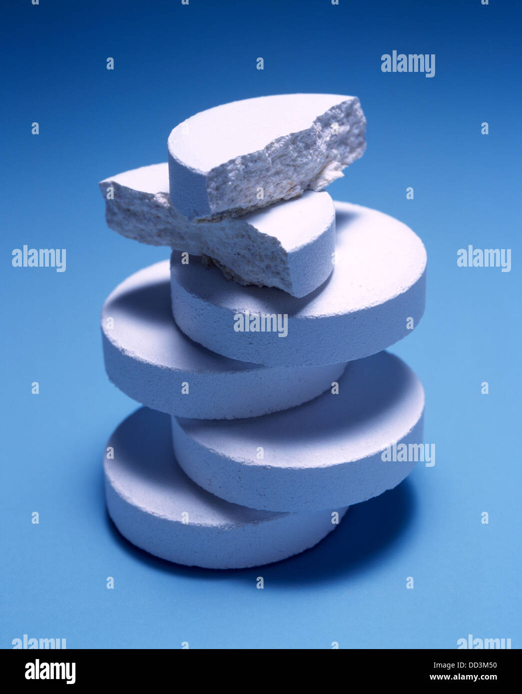 A large stack of white medicine tablets on a blue background. Stock Photo