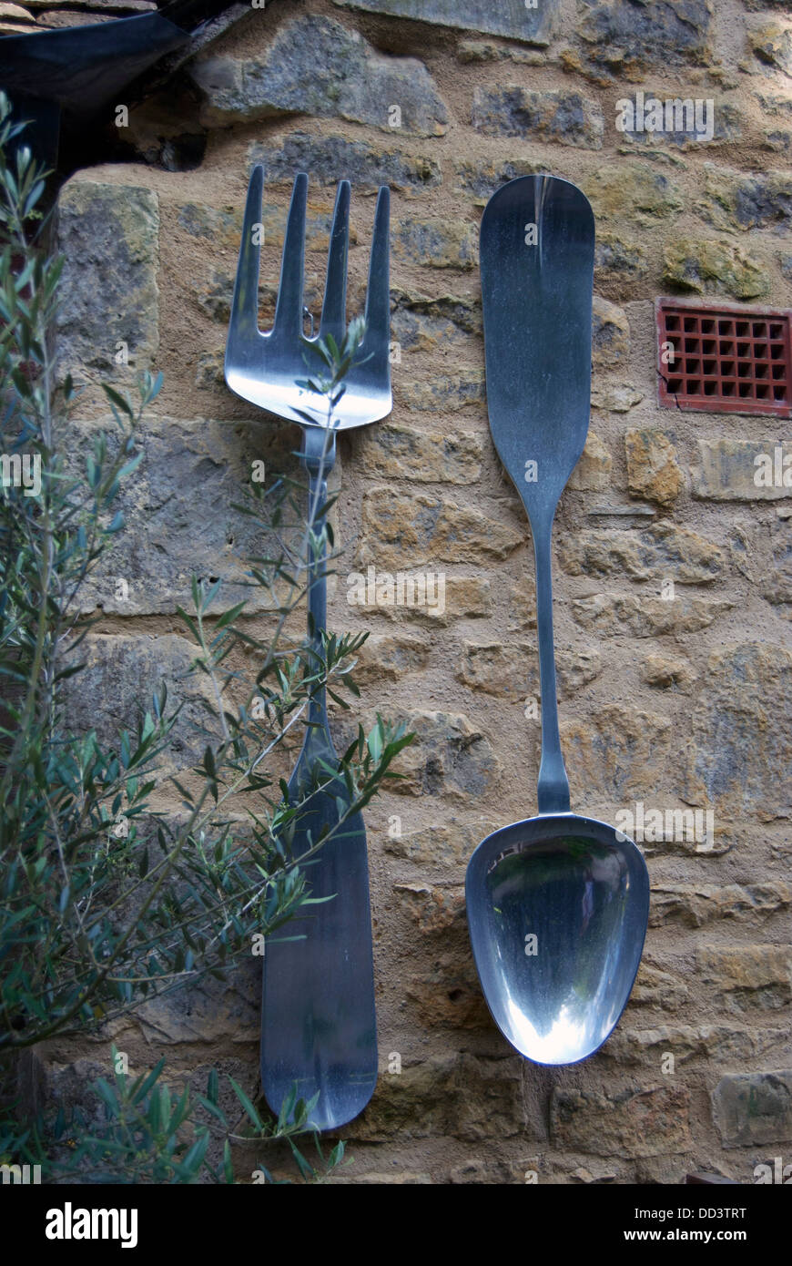 Large metal spoon and fork on old garden wall of restaurant at Hidcote
