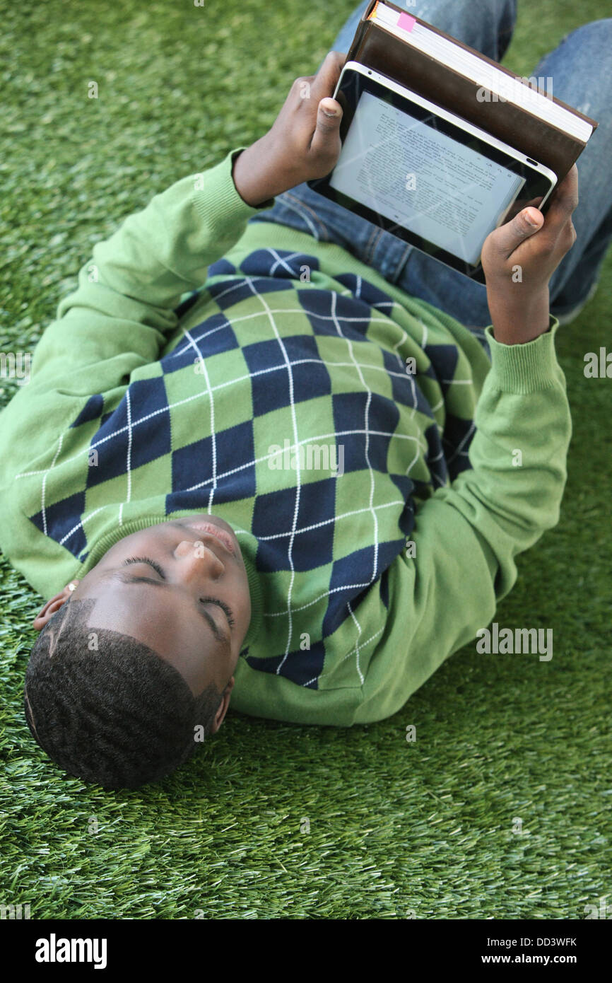 A Boy In An Argyle Sweater Lays On The Grass Reading From An Electronic Notebook; Portland, Oregon, United States of America Stock Photo