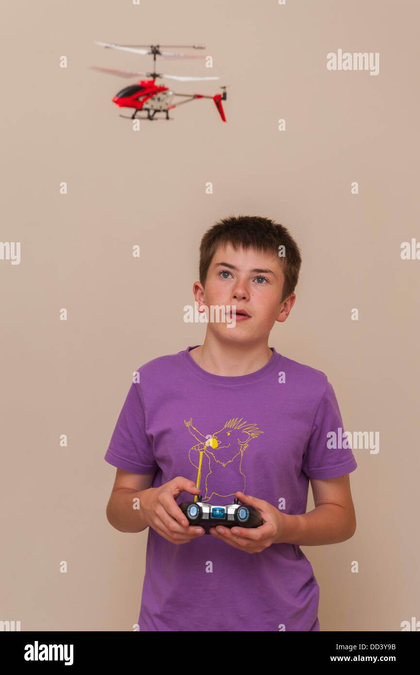 A 13 year old boy flying his radio controlled helicopter indoors Stock Photo
