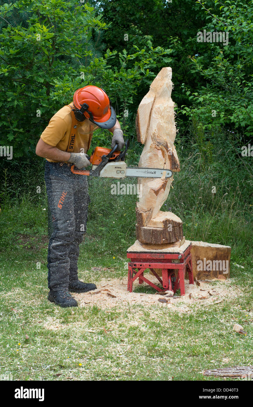 Chainsaw carving, Man carving hare form solid tree trunk Stock Photo