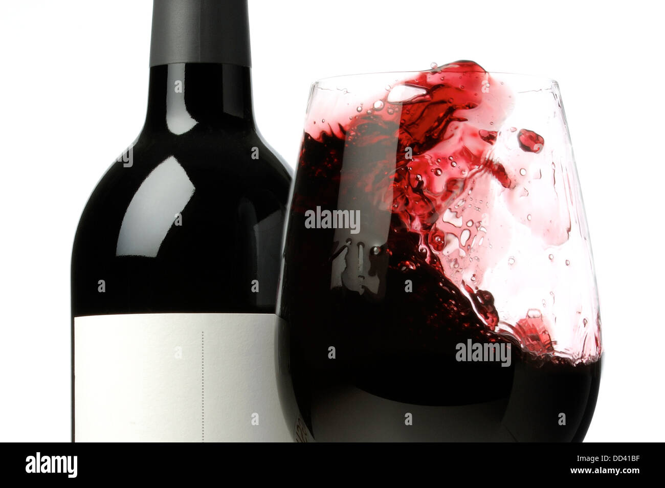 A excited glass of red wine next to a bottle of red wine. Stock Photo