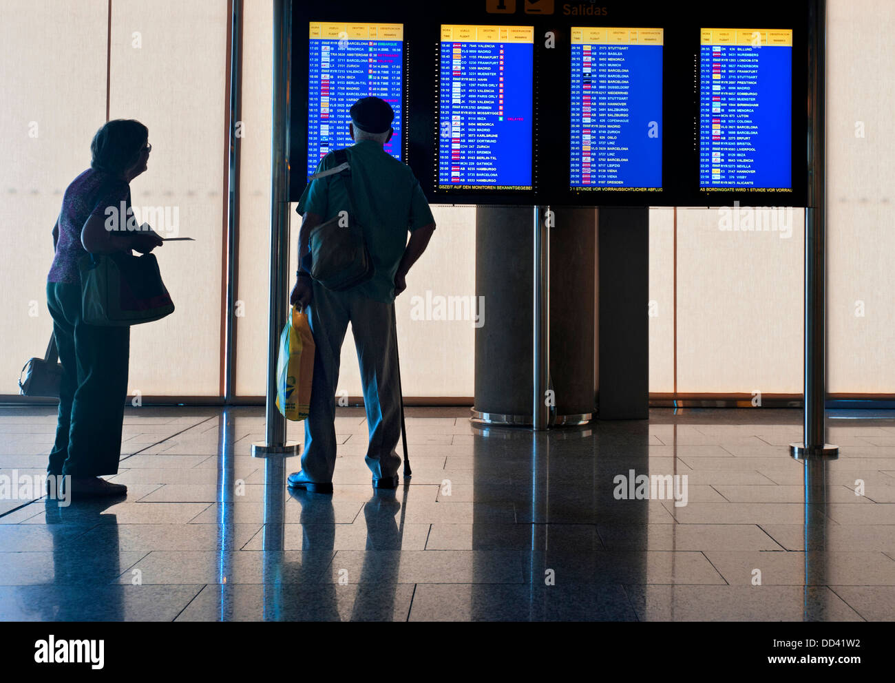 Airport Elderly airline passengers couple travellers standing on airport concourse looking at flight departures information screens Stock Photo