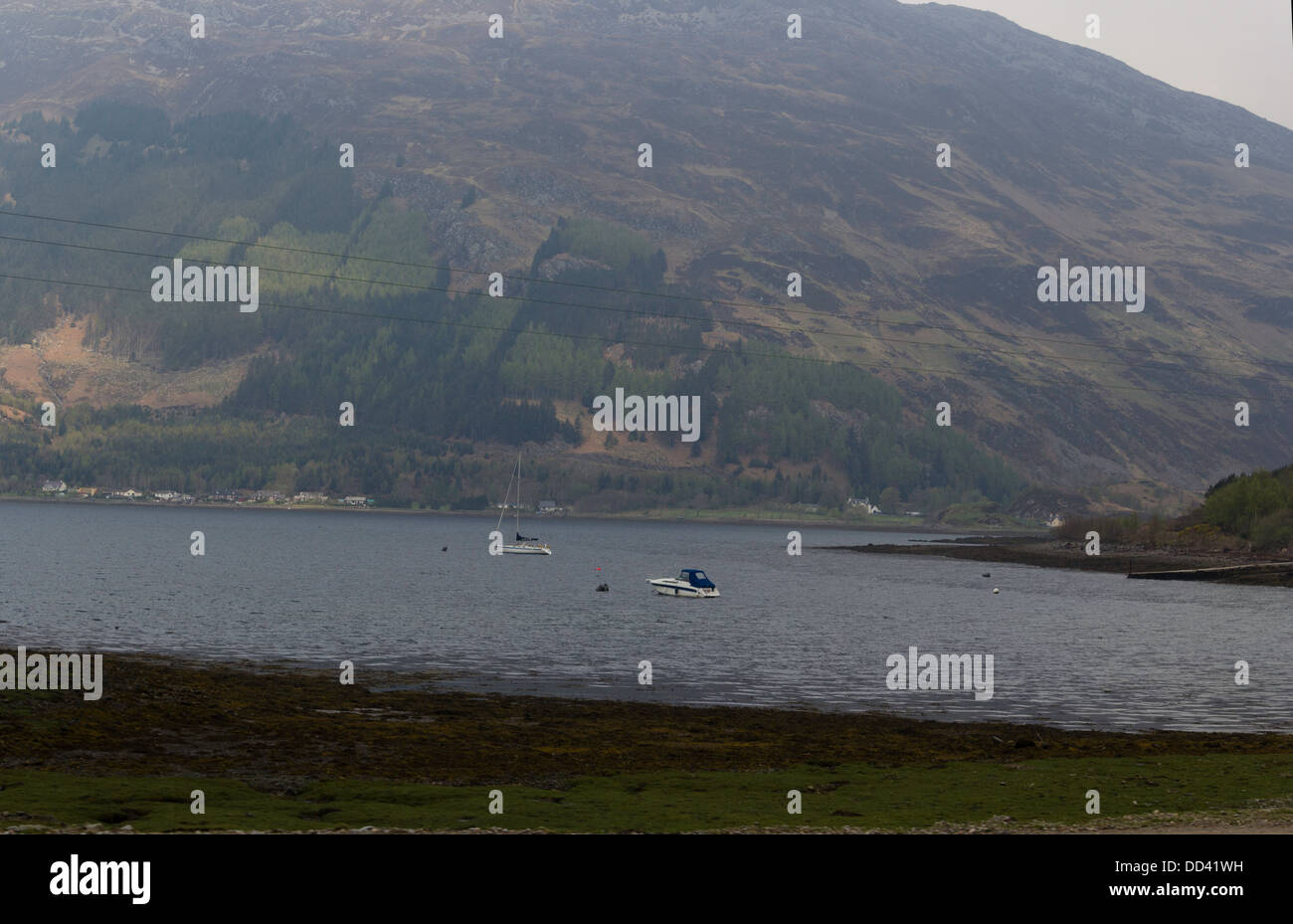 Enjoying with a boat and sailboat in a Loch in the Scottish Highlands. Shore of the lake and hills in background visible. Stock Photo