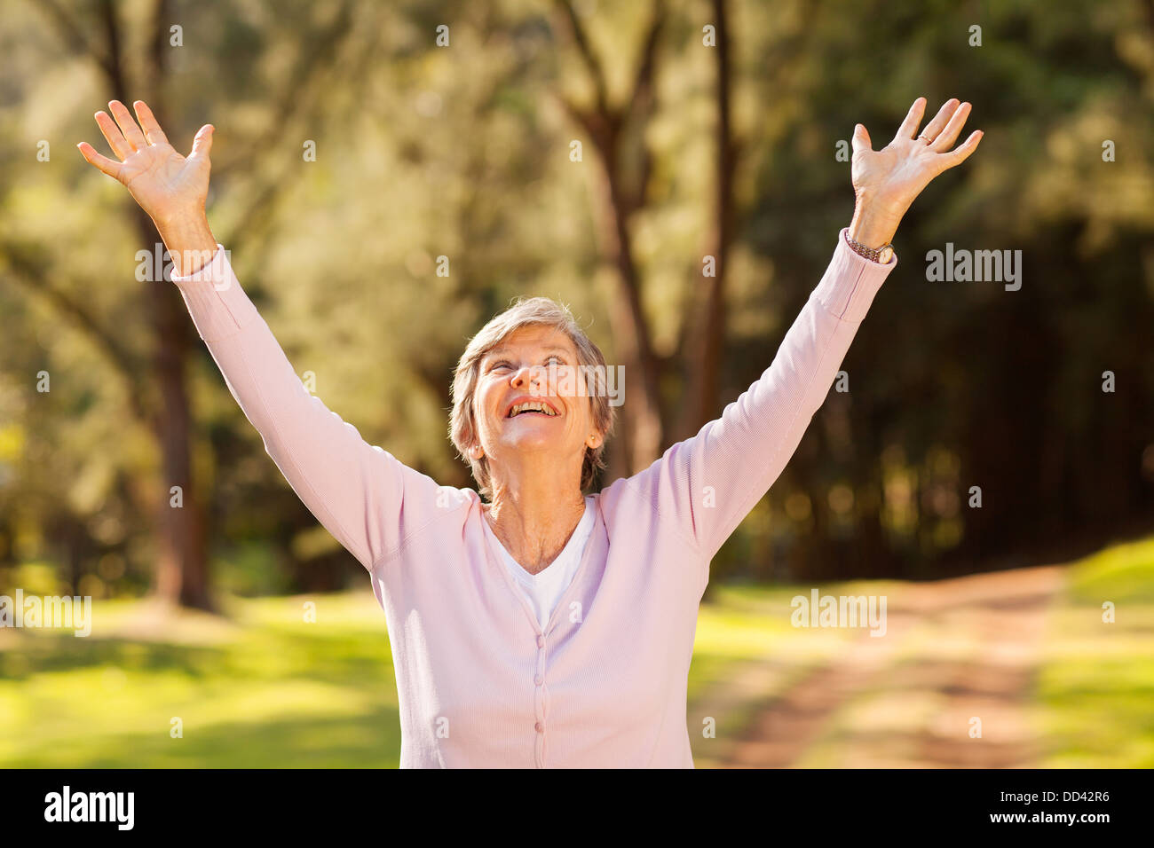 healthy elderly woman looking up with arms outstretched outdoors Stock Photo